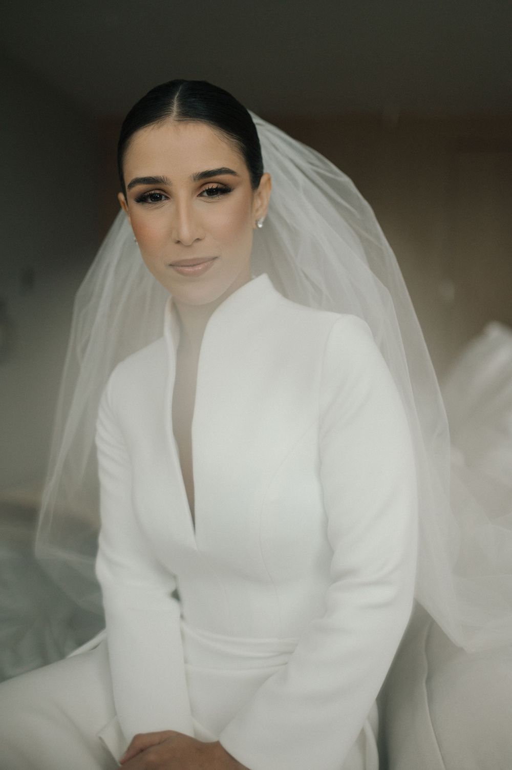 Elegant bride wearing a modern white high-neck wedding gown with structured shoulders and flowing veil.