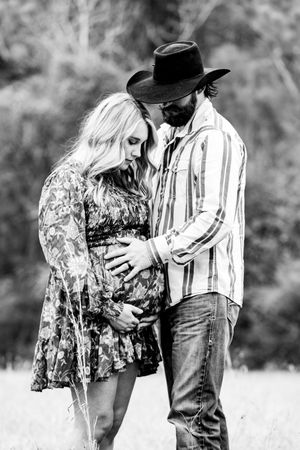 Black and white intimate maternity photo in rustic outdoor setting.