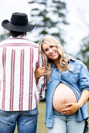 Expecting couple in casual denim and stripes pose outdoors.