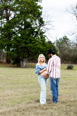 Wide landscape shots of a couple standing together in a grassy field surrounded by trees.