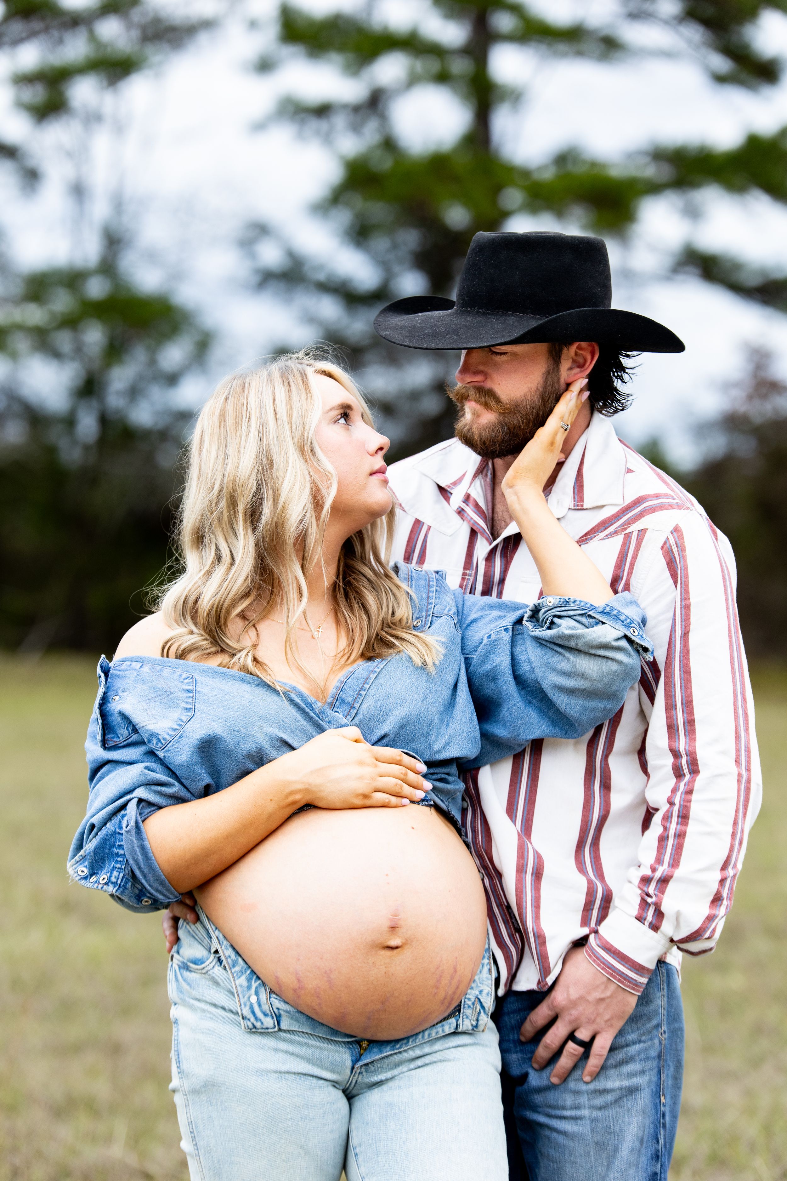 Couple in western wear sharing tender moments in a sunlit meadow.