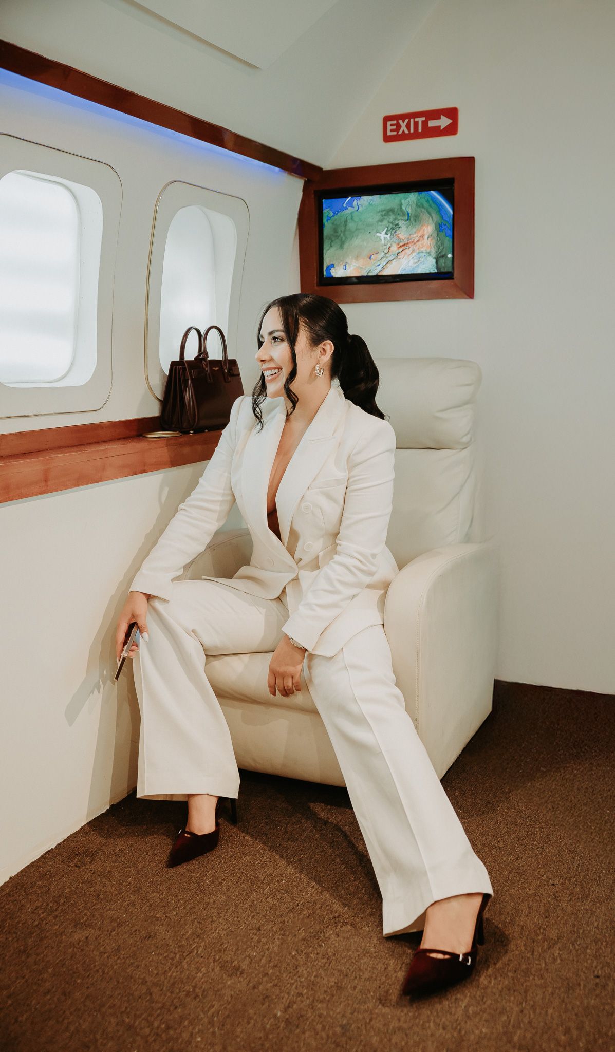 Person wearing white suit sits on beige leather bench seating in what appears to be luxury transportation interior.