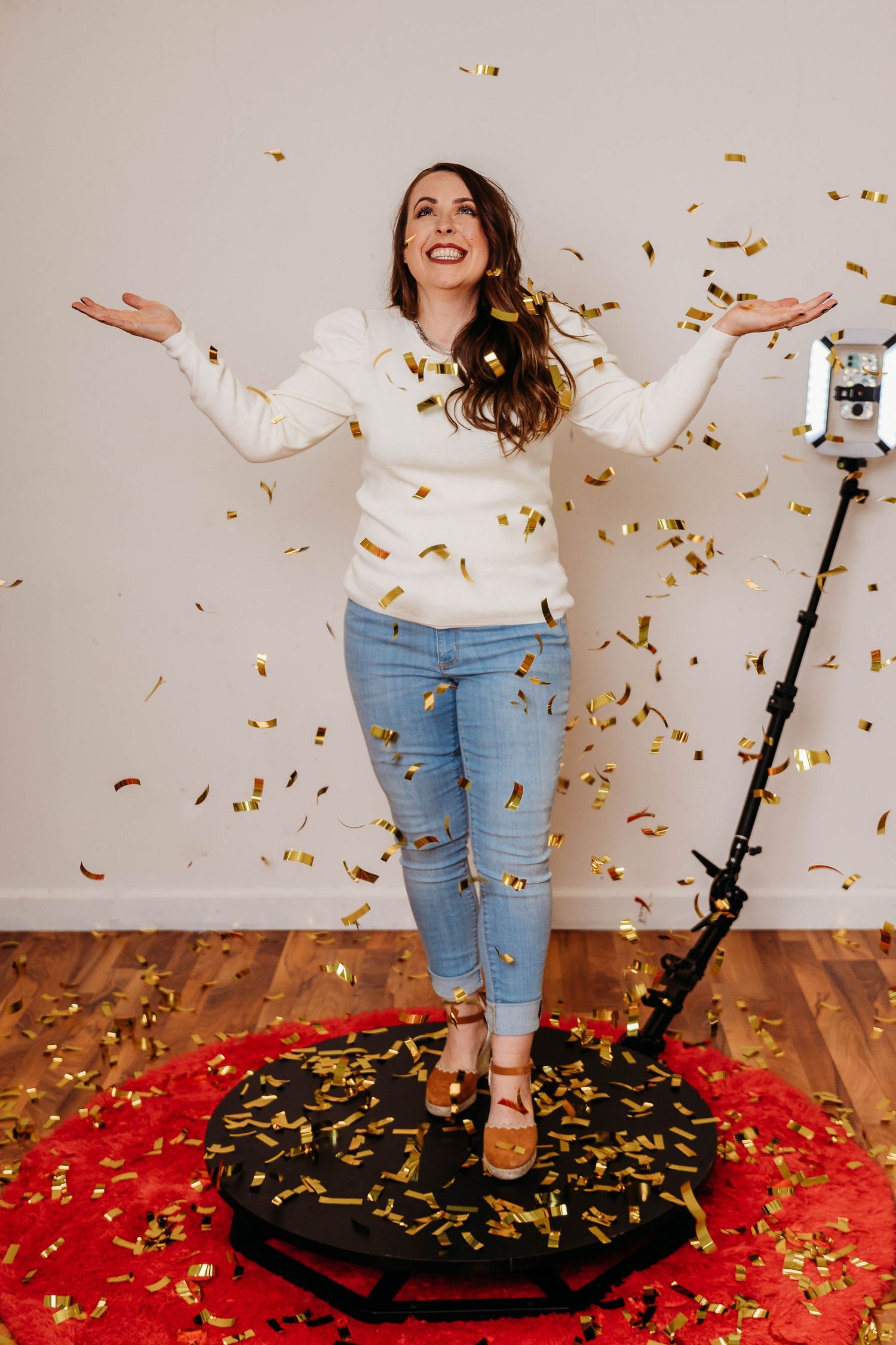 A joyful moment captured with gold confetti falling and a red carpet on hardwood floors during a celebratory photoshoot.