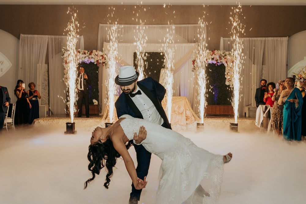 Couple performs romantic dip during their first dance at wedding reception with sparklers and white decor at Babylon Palace.