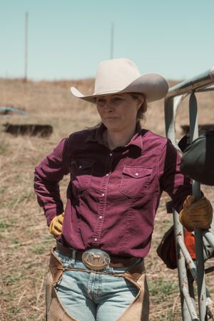 Rancher in pink shirt and cowboy hat standing by vehicle on prairie.