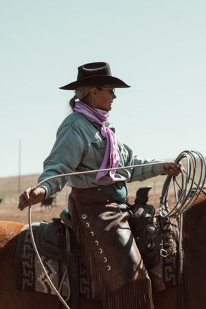 Cowboy in traditional western wear sitting mounted on horseback against light sky.