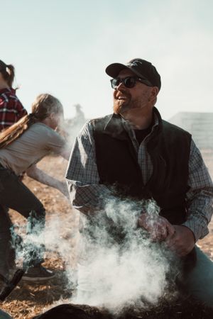 Ranch worker takes a break amid rising smoke during cattle work.
