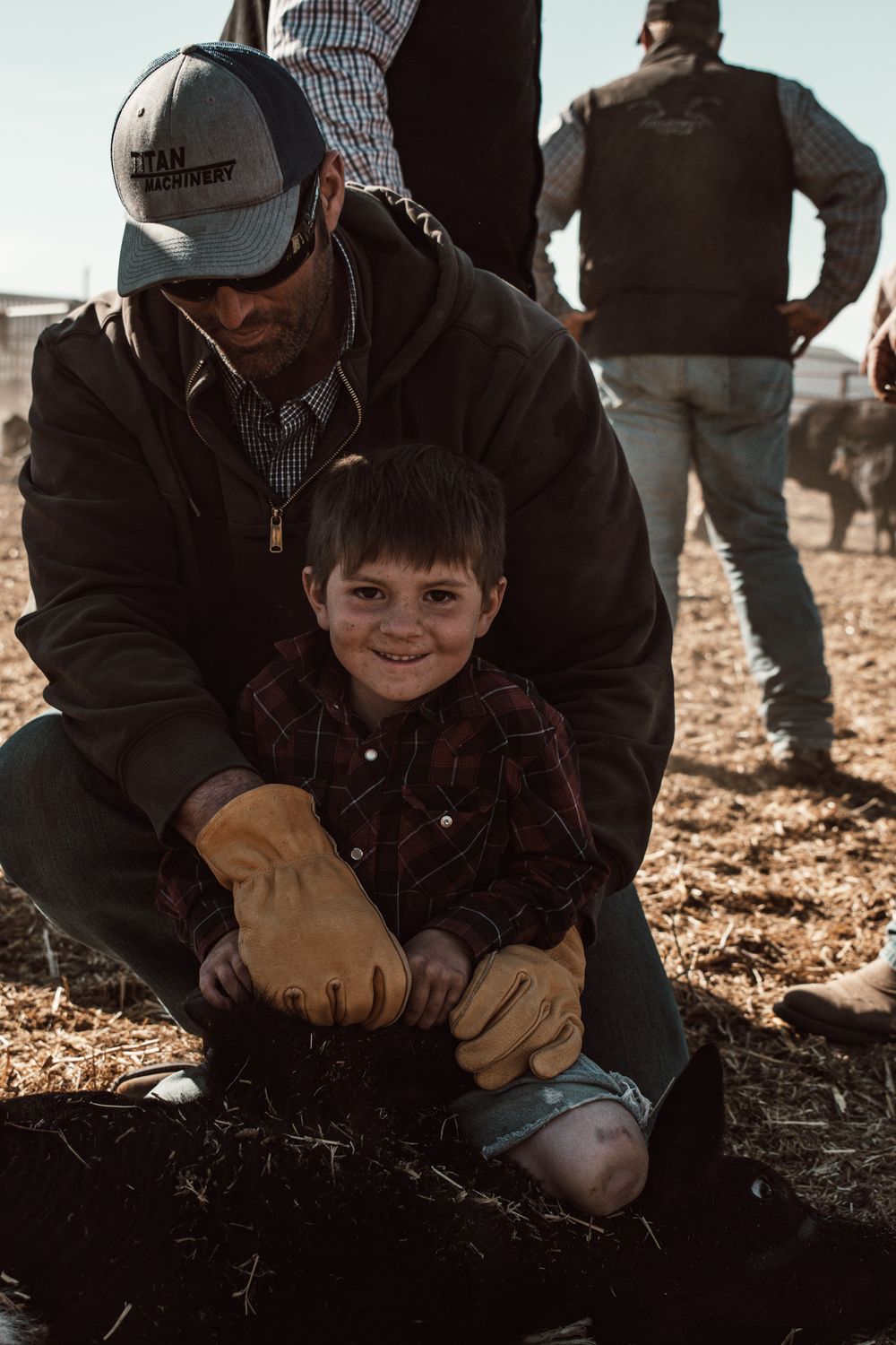 A heartwarming teaching moment between an adult and child on a ranch during a sunny day.