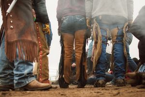 A row of people wearing western boots and jeans standing in line at a country event.