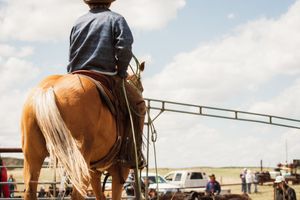 Closeup of western horseback riders wearing chaps and boots competing in a rodeo arena on a sunny day.