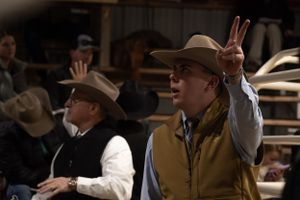 Two people in western attire at indoor event with one making peace sign gesture.