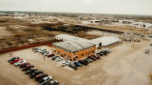 Aerial view of a brick commercial building with parking lot surrounded by industrial development in a rural area.
