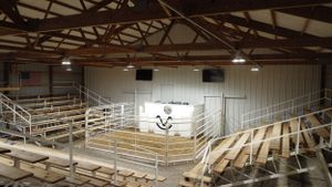 Indoor livestock arena with empty bleachers and white wall panels.