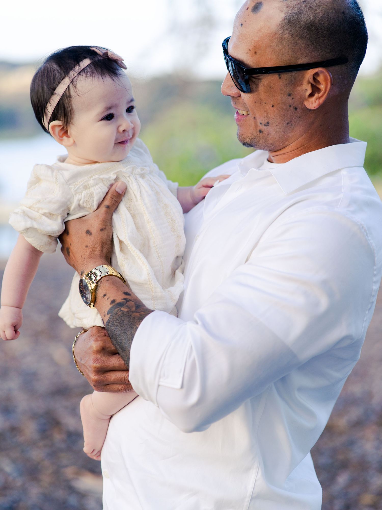Sweet moment between parent and baby wearing white outfits outdoors.