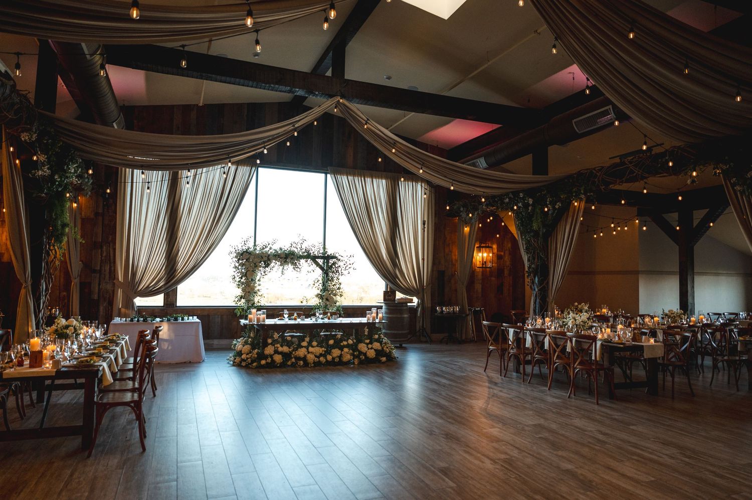 View of the Farmview Ballroom at The Barn at Villa Venezia in Middletown, NY with exposed beams, tables set for reception, string lights.