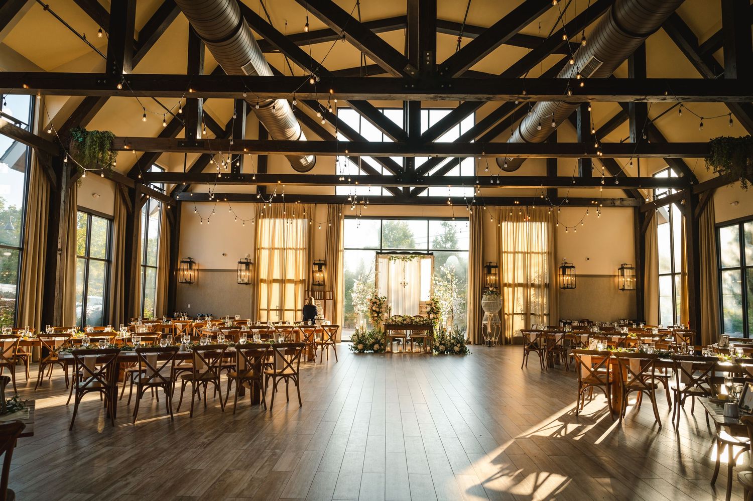 View of the Cypress Ballroom at The Barn at Villa Venezia in Middletown, NY with exposed beams, tables set for reception, large windows.