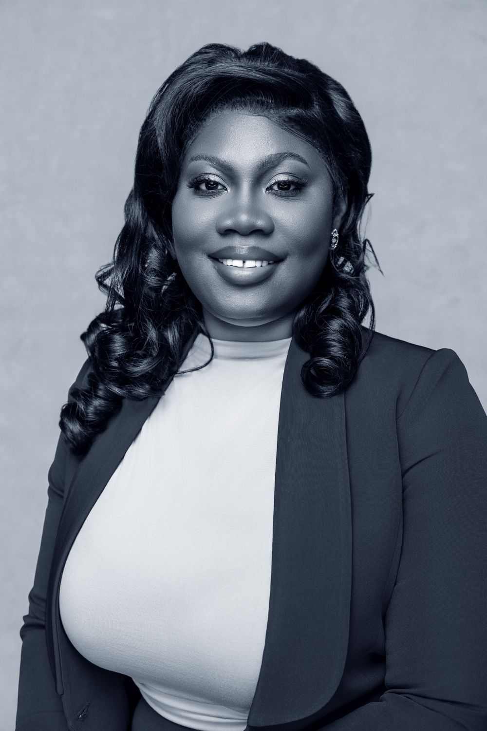 Professional black and white portrait of a smiling businesswoman in a blazer with curly hair.