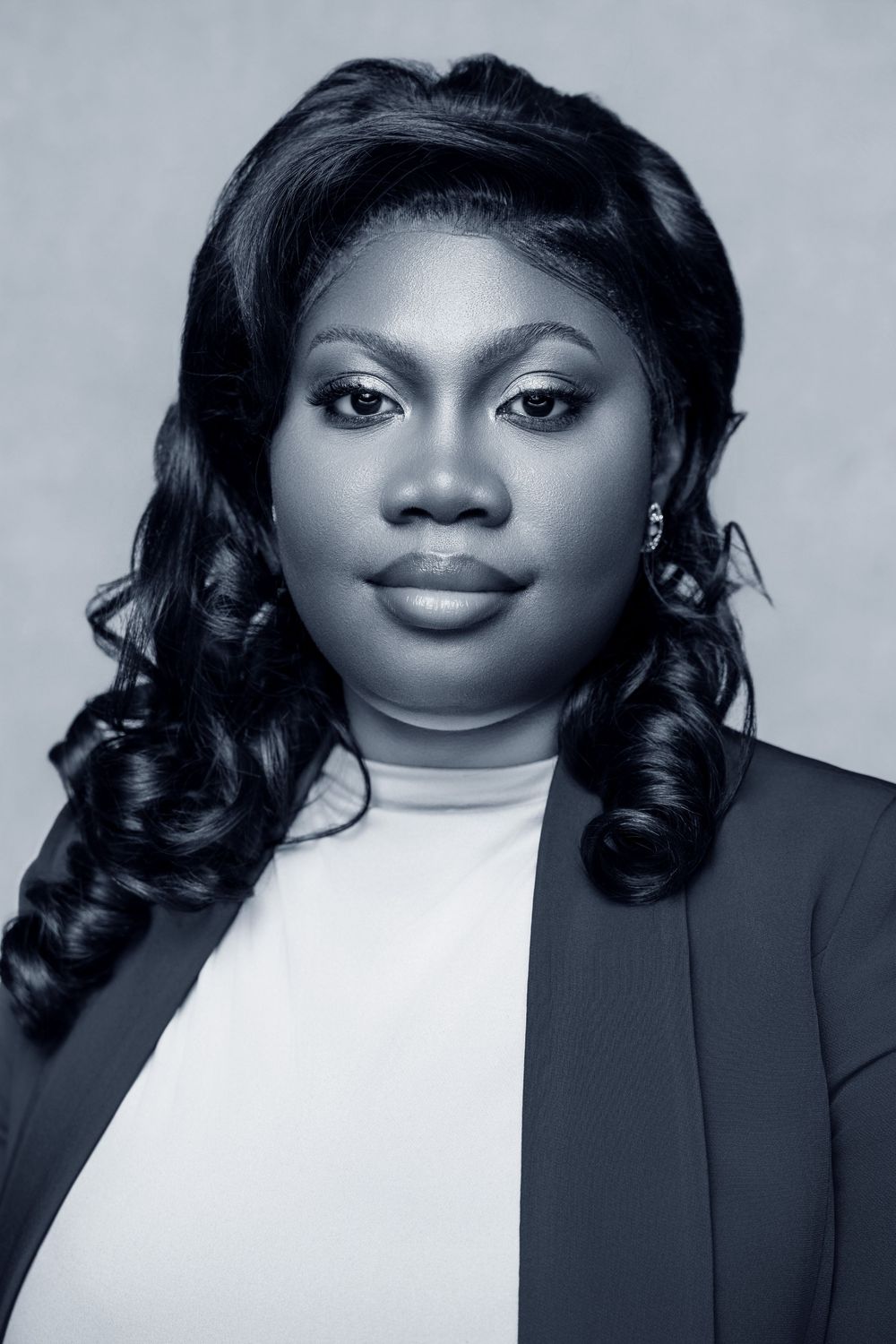 Professional black and white portrait of a young woman in a blazer with elegant curled hair and earrings.