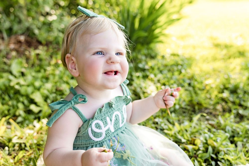 A series of photos showing a baby in a teal dress sitting outdoors in a lush garden setting.