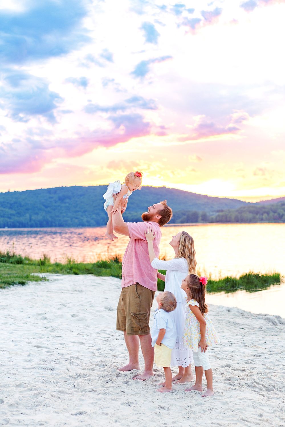 A family enjoying a beautiful sunset moment together on a beach with mountains and colorful sky in the background.