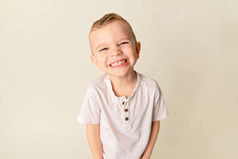 Happy expression on young child wearing white henley shirt against beige background.