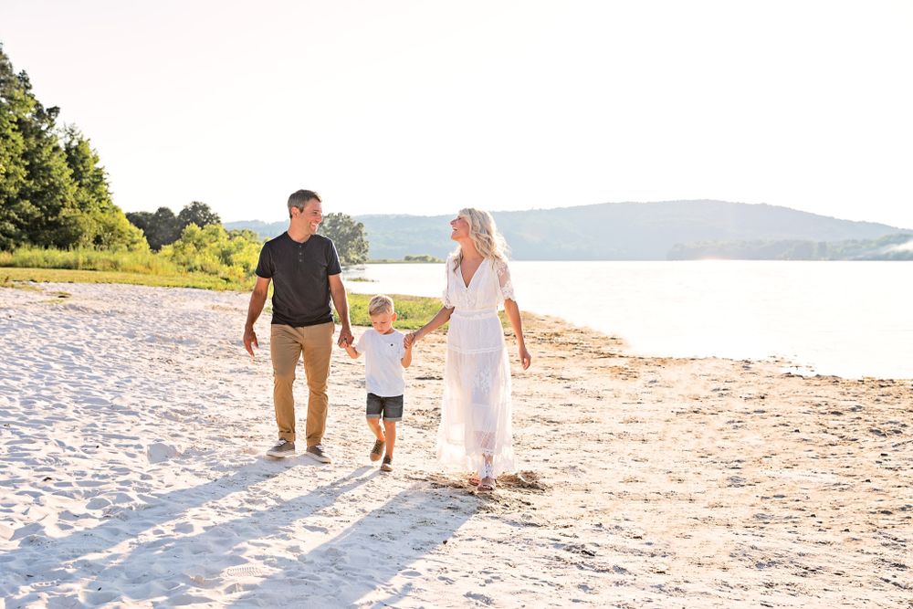 Family walking together on sunny white sand beach with water view.