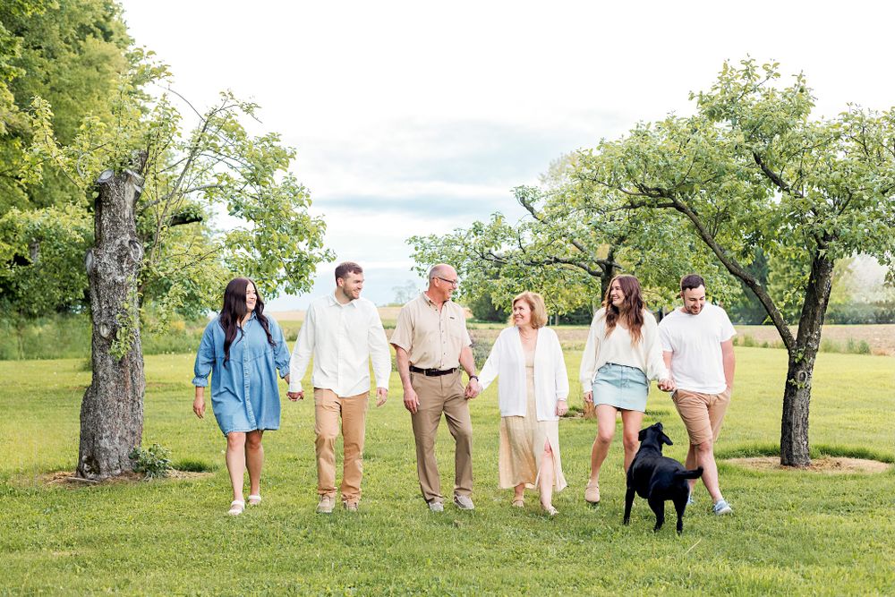 A group of people and a black dog walking together on a grassy lawn with trees in the background on a sunny day.