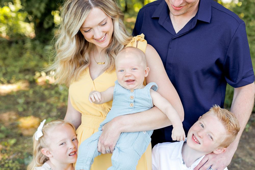 Cheerful outdoor family portrait with yellow dress and navy polo shirt in summer setting.