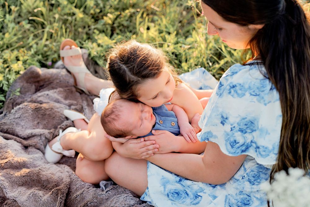 Tender moment on a blanket outdoors with a blue floral dress visible in golden sunlight.