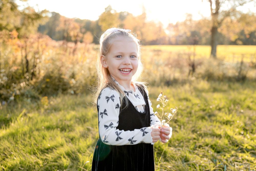 Child holding wildflowers while wearing a black and white patterned outfit in a sunny field.