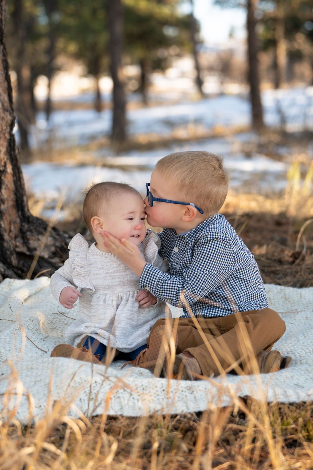 Sweet moment between two young children sitting on blanket in snowy forest setting.
