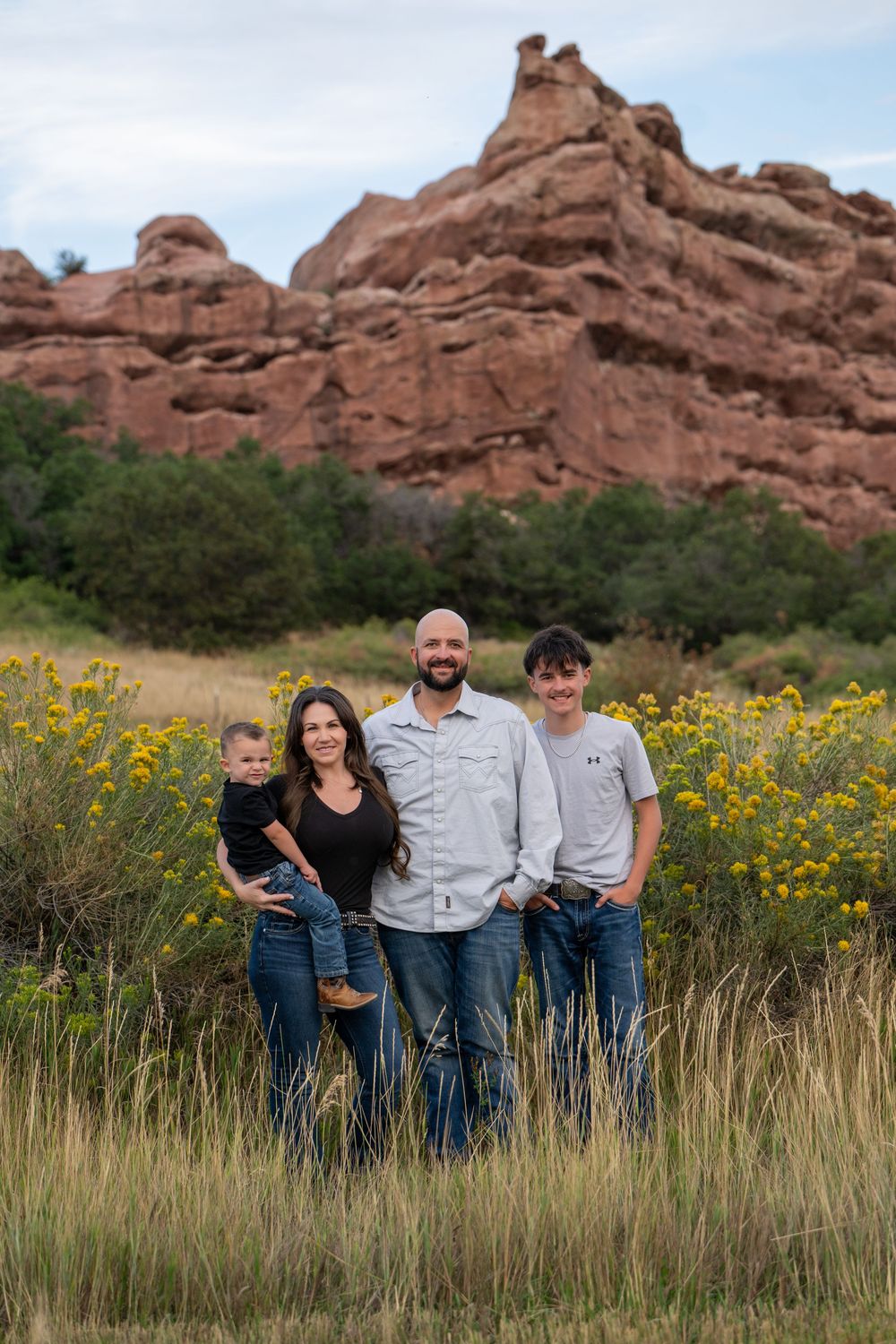 A group stands in a meadow of yellow wildflowers with dramatic red rock formations at Arches National Park in the background.