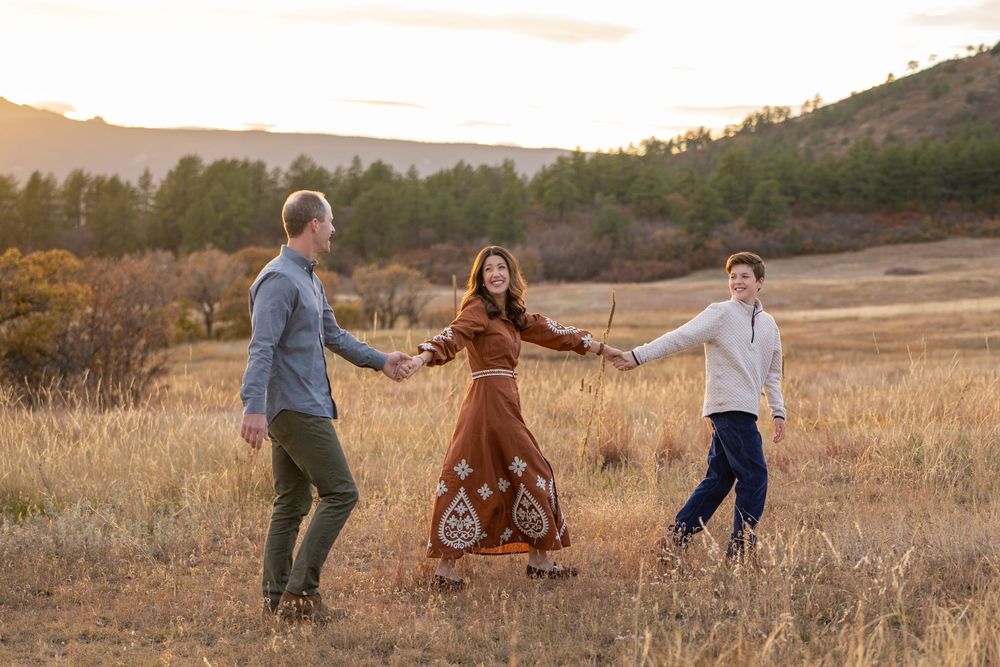 A family plays together in a golden autumn field at sunset as their dog runs alongside them.