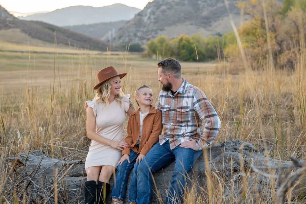 Family in casual western wear sitting together on rocks with mountain landscape behind them.