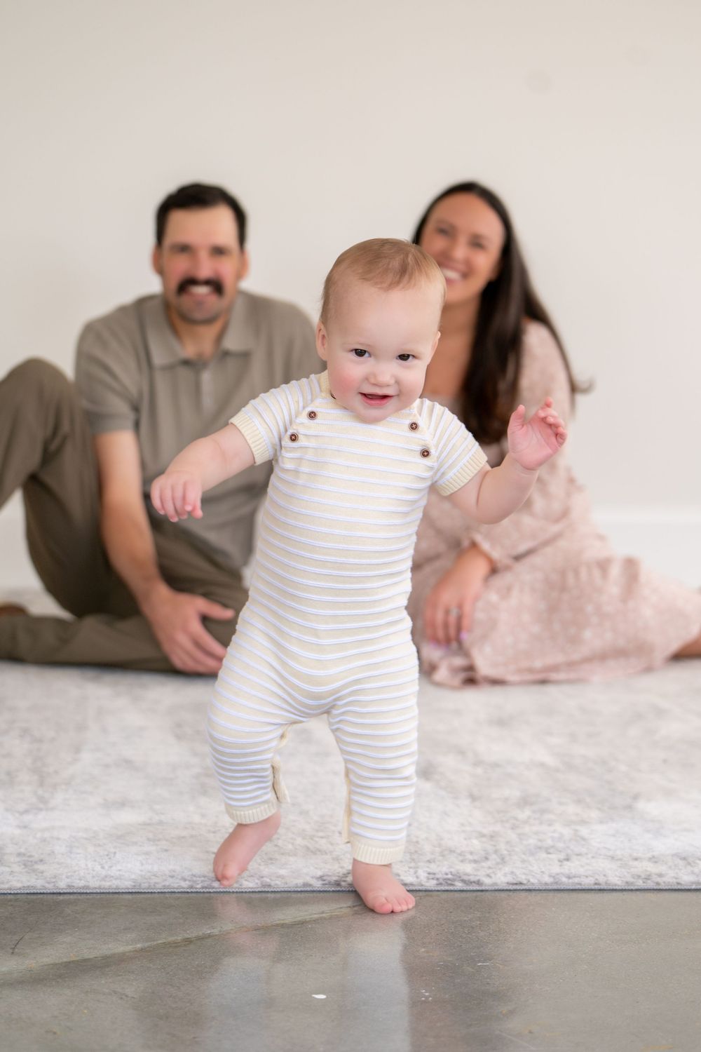 A sequence of photos showing a baby's progression from lying down to standing while wearing a striped onesie.