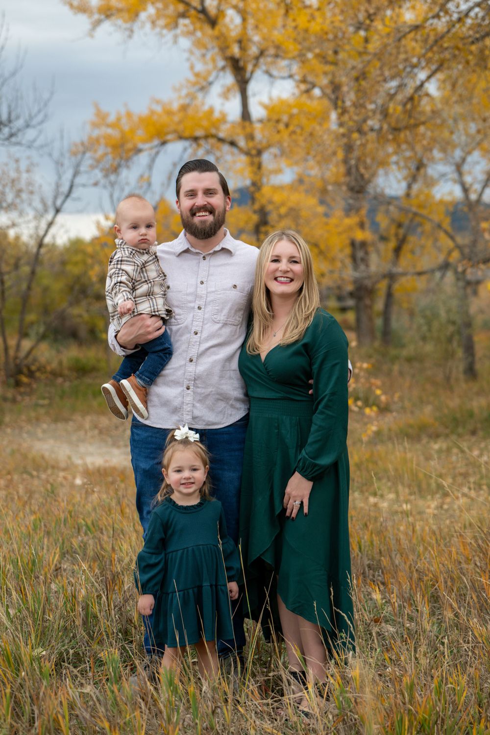 Family of four in coordinating green outfits posed together in autumn field setting.