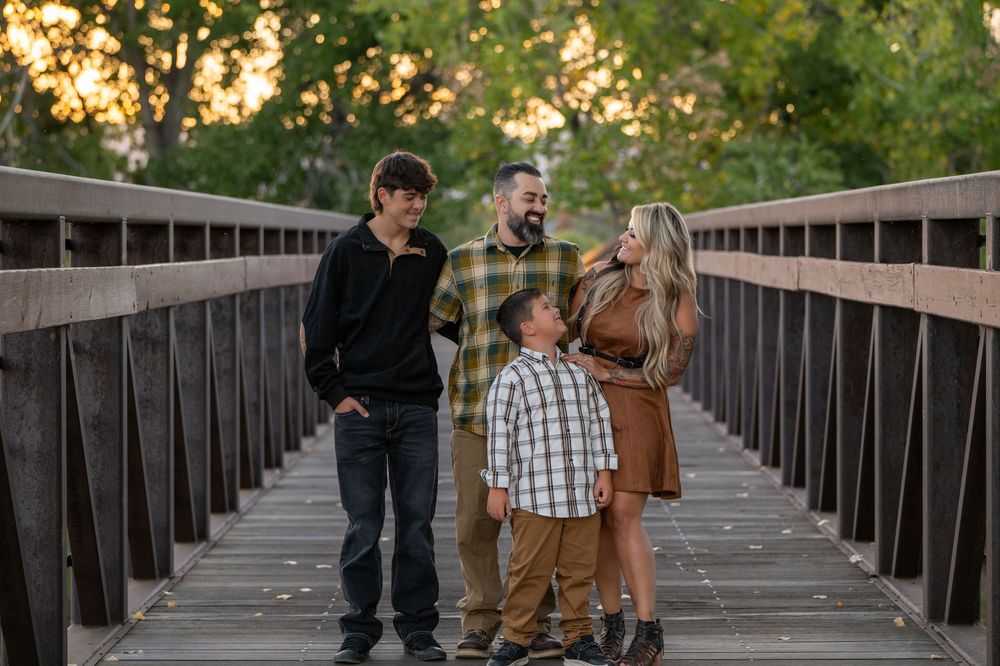 Three people walk and talk together on a wooden footbridge at sunset.