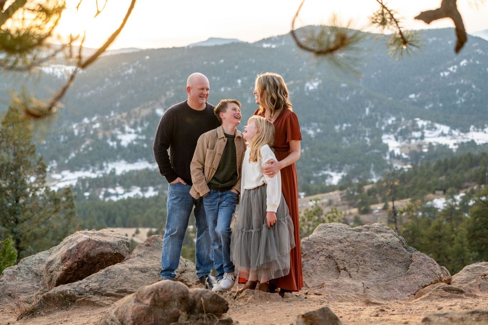 Family of three standing together on mountain overlook with snow-capped peaks in background.