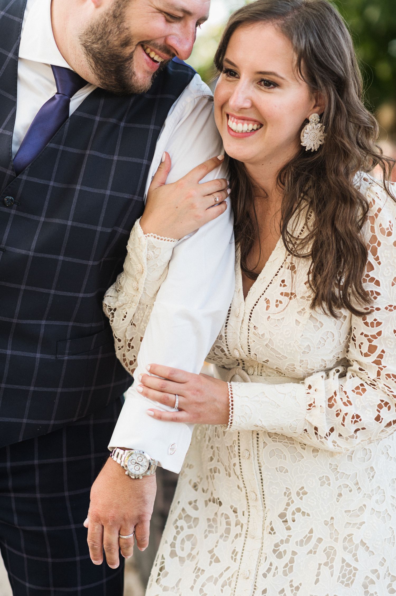 A couple sharing a joyful moment on their wedding day, with the bride wearing an elegant lace dress and beaming smile.