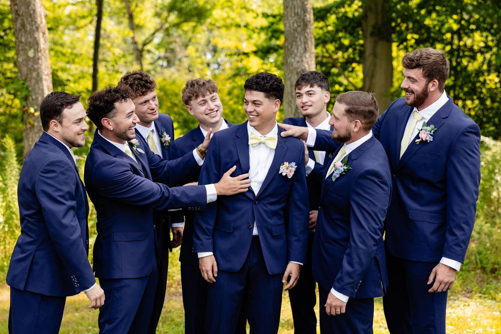 Groomsmen in navy blue suits laughing together outdoors at a wedding ceremony.