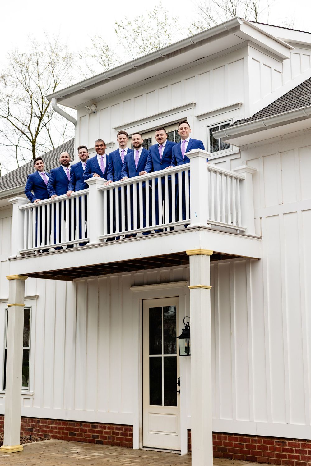 Groomsmen in blue suits and pink ties pose on a white balcony of a elegant wedding venue.