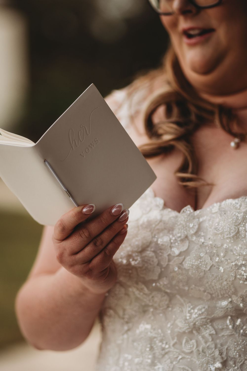 Close-up of hands holding a small white book or card, with lace wedding dress detail visible.