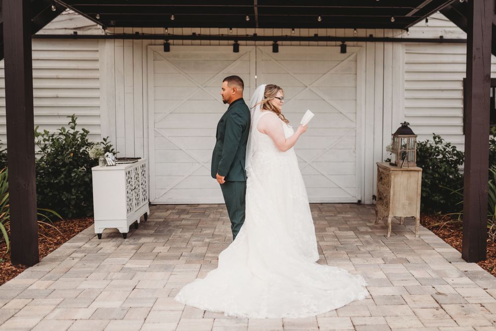 Couple in wedding attire stand back-to-back reading letters on stone patio.
