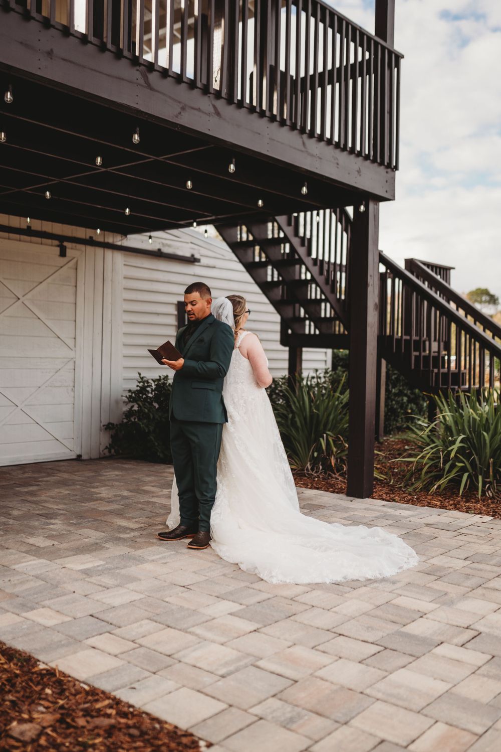 Wedding couple reading letters while standing back-to-back under wooden deck structure.