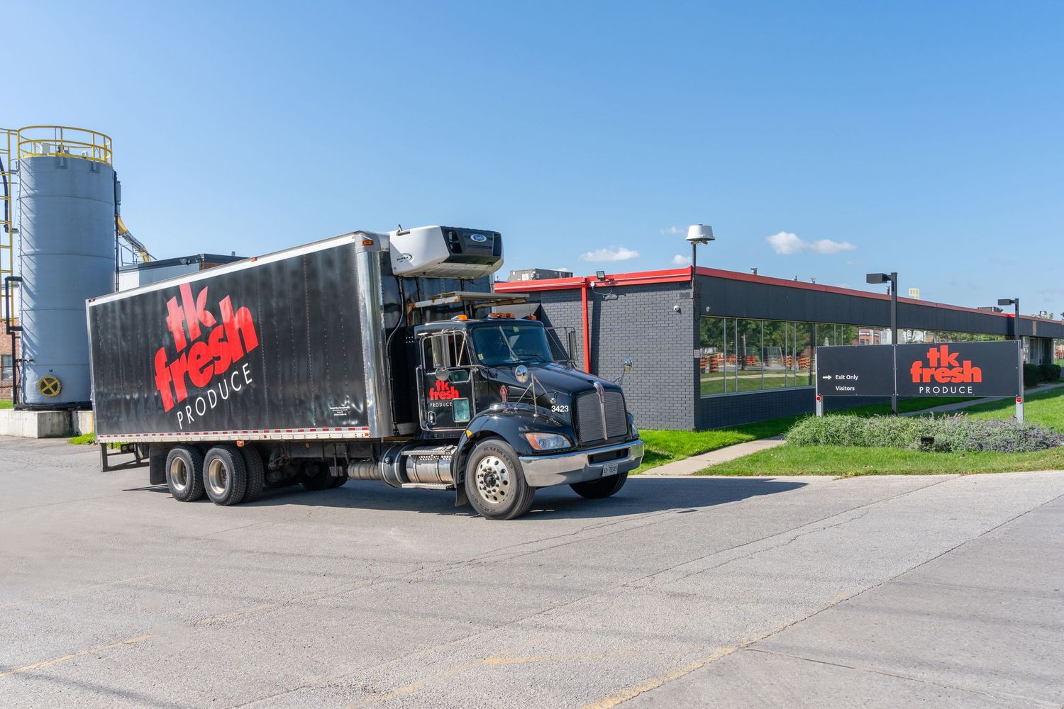 Fleet of commercial trucks and trailers parked at a distribution center under blue sky.