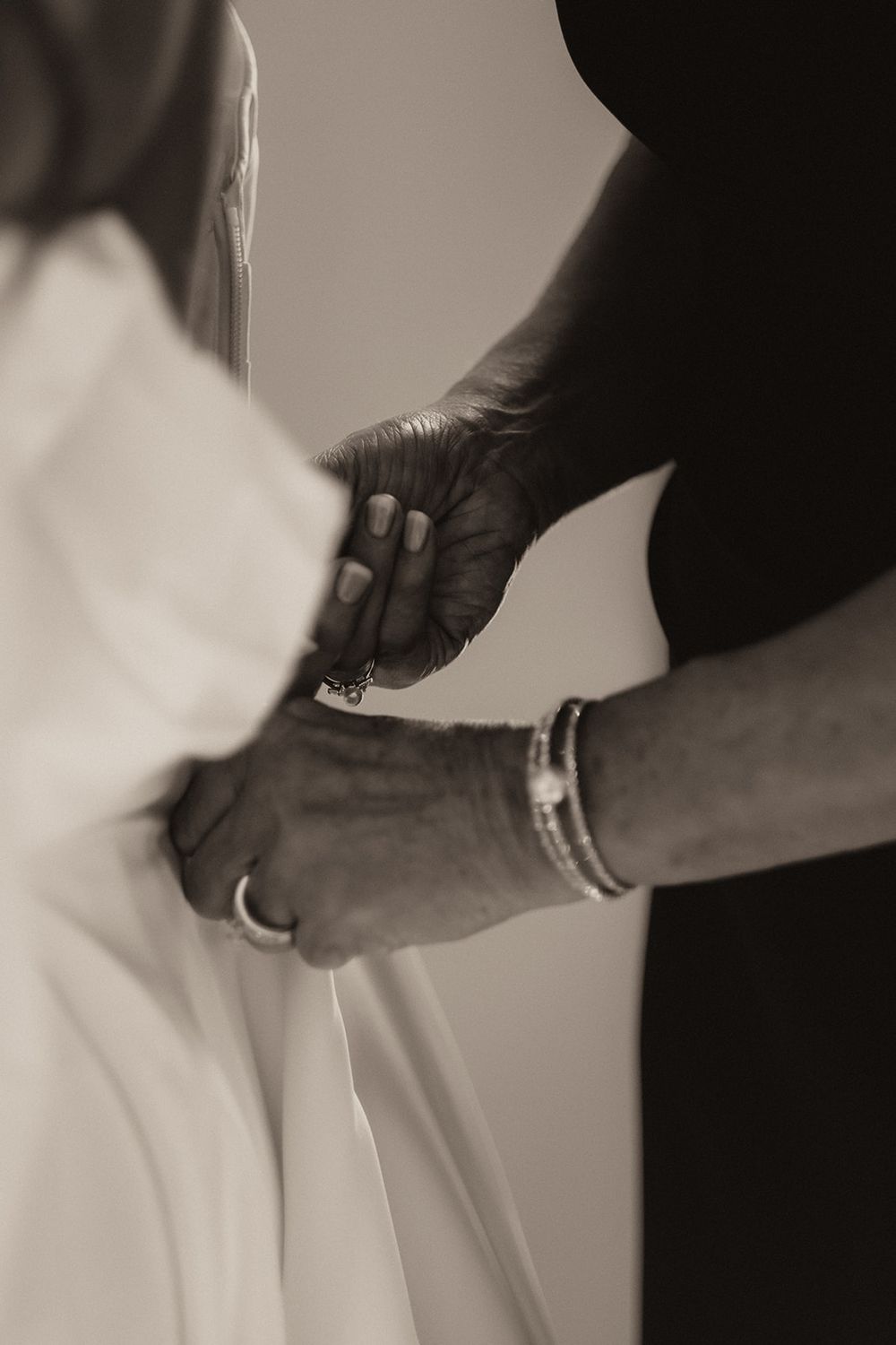 Sepia toned close-up of hands fastening bride's wedding dress buttons before ceremony.