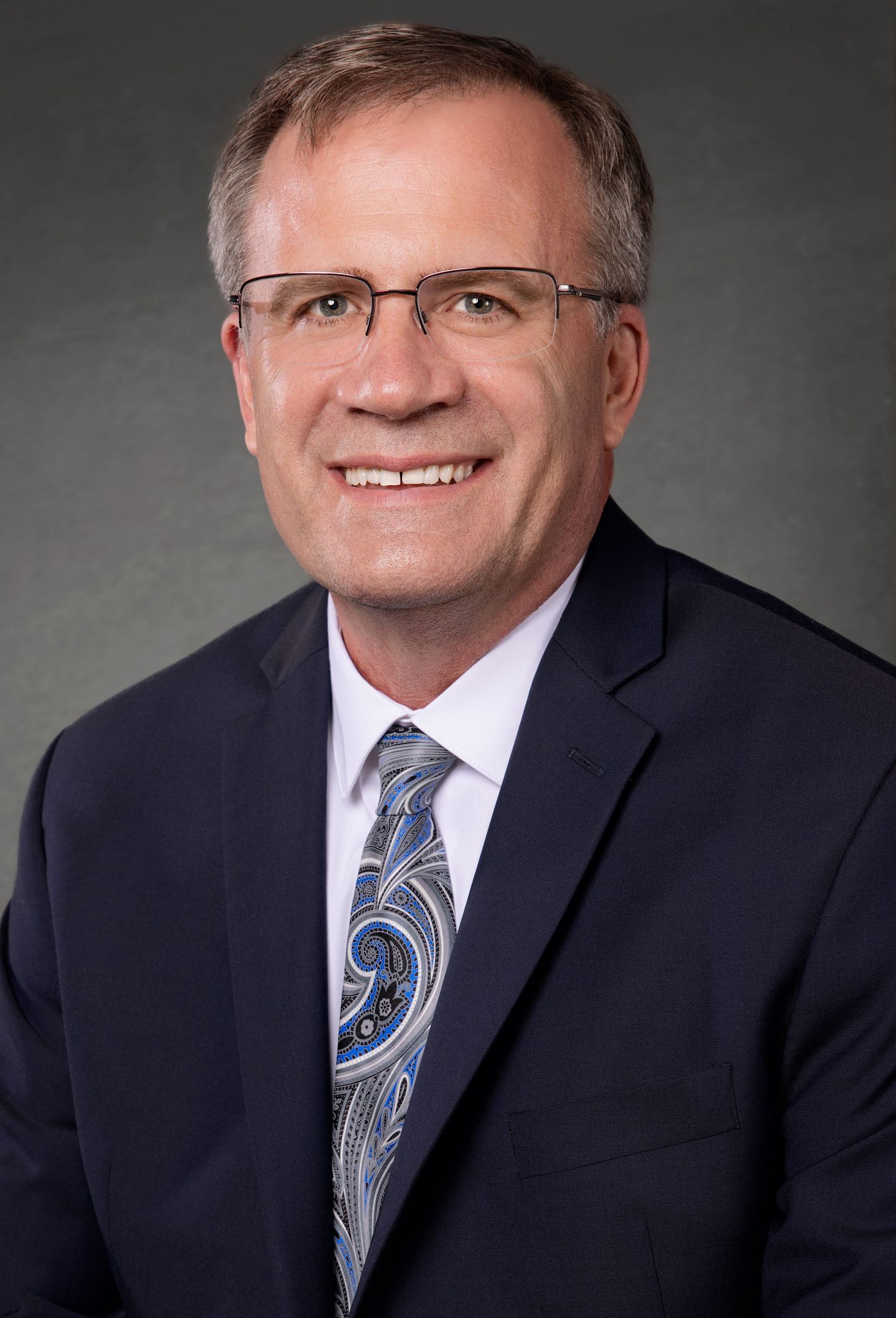 Professional business portrait featuring man in dark suit with blue paisley tie.