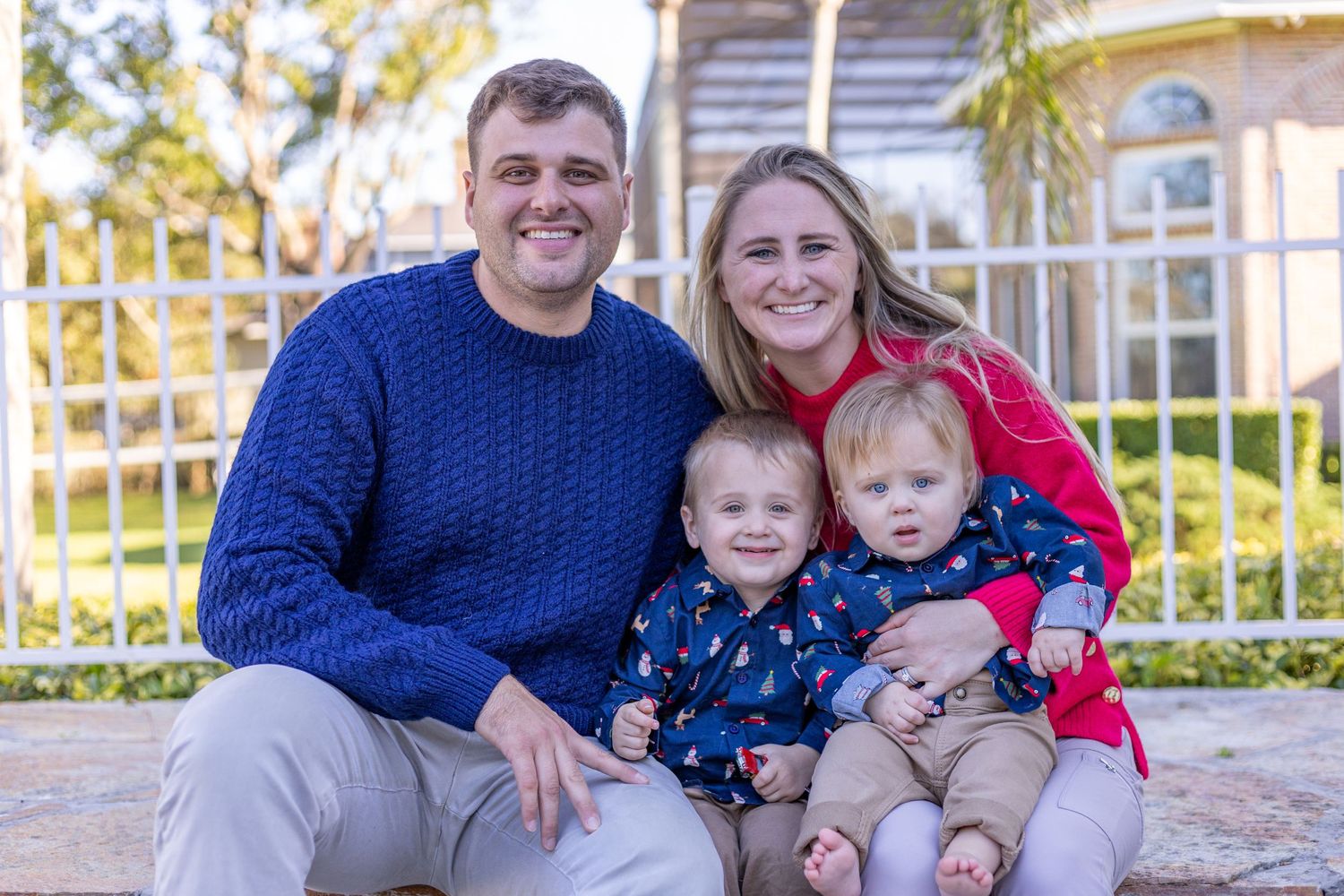 Happy family with two toddlers posing outdoors in front of house.