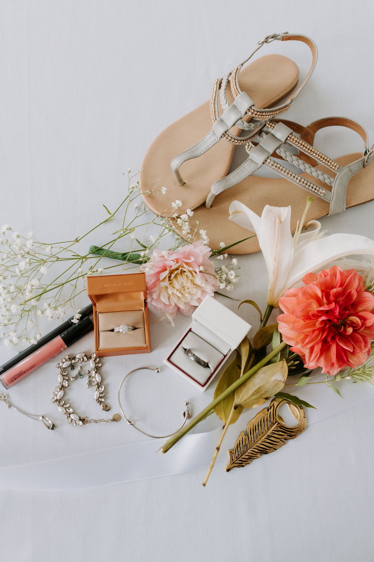 Wedding accessories flatlay with sandals, rings, flowers and jewelry on white background.