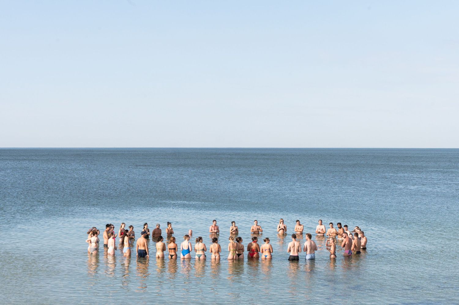A group of people standing in formation in shallow ocean water against a serene blue horizon.